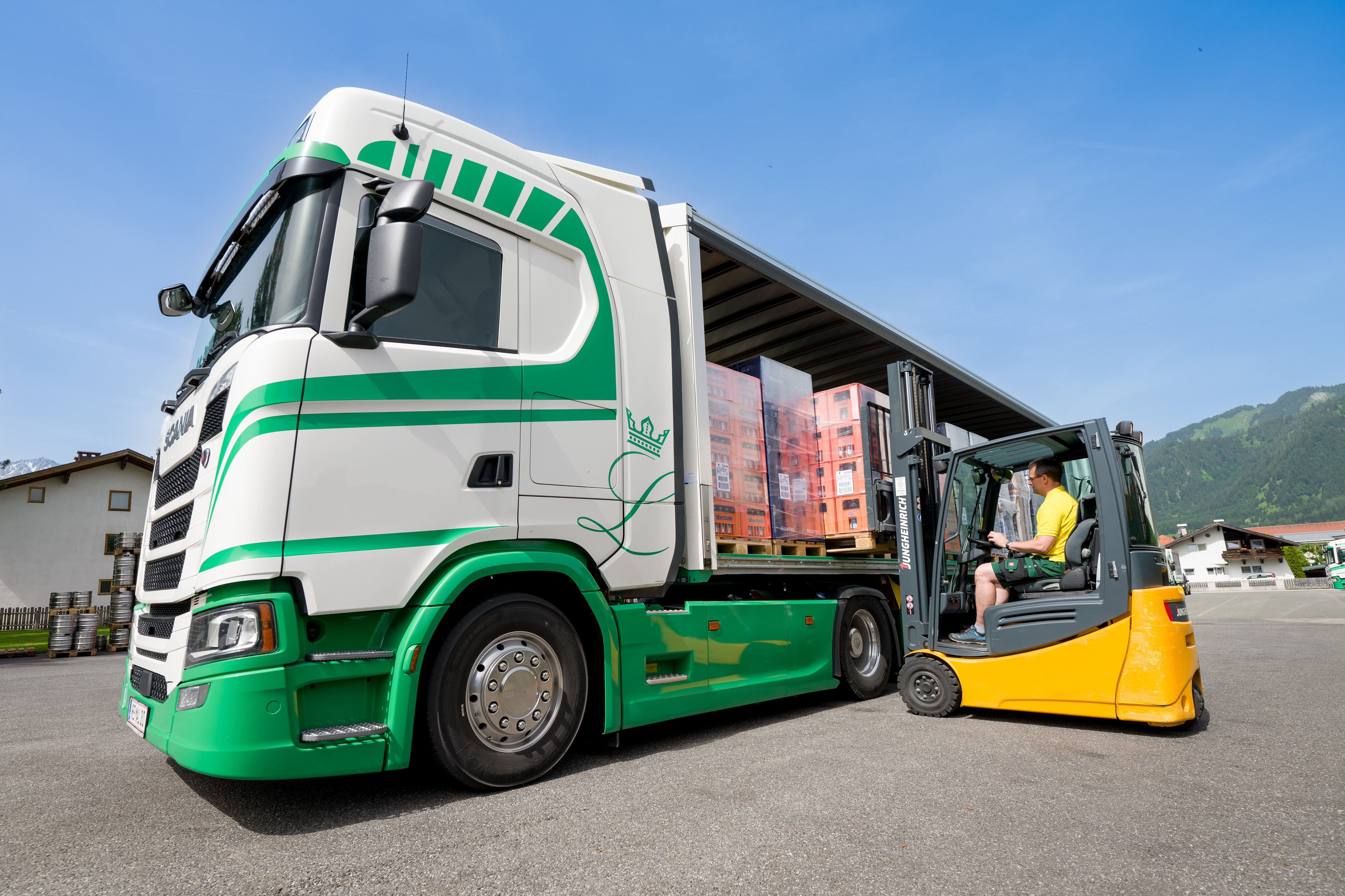 Fokus auf einen Linzgieseder-LKW und einen Gabelstapler im Mittelpunkt, die beim Beladevorgang zu sehen sind. Im Hintergrund ist ein blauer Himmel.