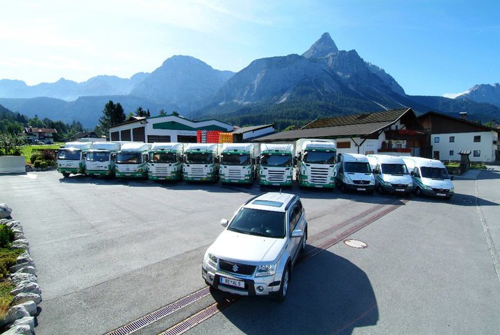 Die LKW- und Sprinterfuhrparkflotte von A. Linzgieseder Getränkehandel ist auf dem Foto zu sehen, im Vordergrund ein PKW. Der Hintergrund wird von einem atemberaubenden Bergpanorama mit der Sonnenspitze geprägt