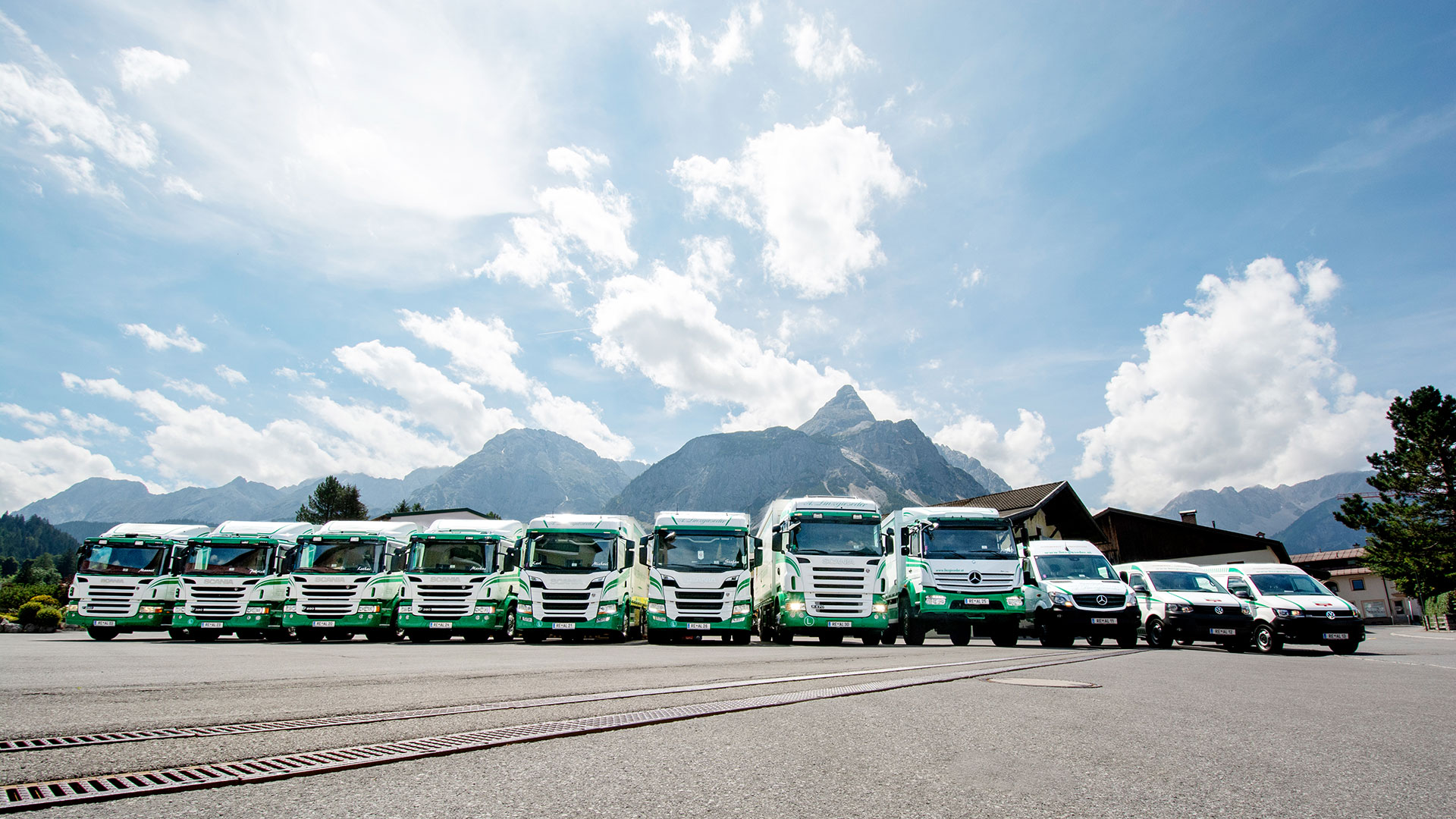 LKW-Flotte von Linzgieseder im Weitwinkel fotografiert, mit der Sonnenspitze im Hintergrund und einem leicht bewölkten blauen Himmel.